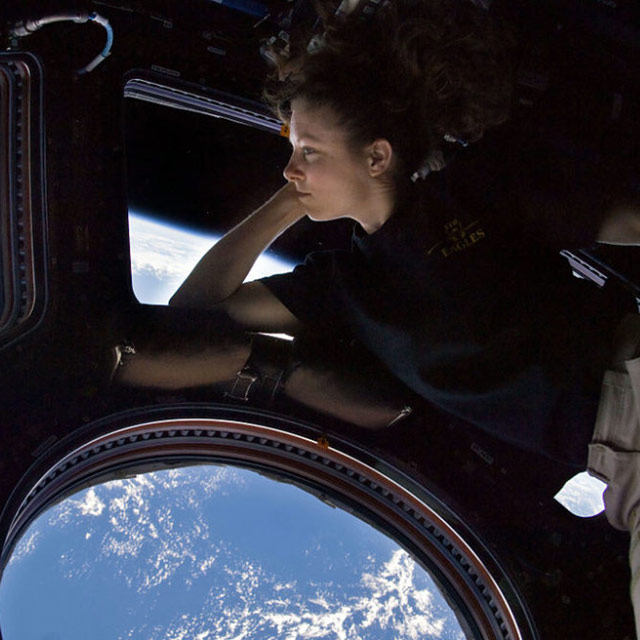 ISS024 E 014263 (11 Sept. 2010) NASA astronaut Tracy Caldwell Dyson, Expedition 24 flight engineer, looks through a window in the Cupola of the International Space Station. A blue and white part of Earth and the blackness of space are visible through the windows.