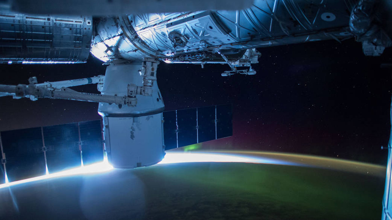 This night image from the International Space Station shows the sun beginning to peak above the horizon sparkling through a green Aurora and reflecting a blue reflection off the station on Apr. 18, 2015 during Expedition 43.