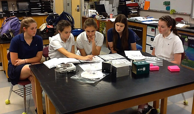 Three years after they first designed their plant growth experiment, high school juniors at Duchesne Academy of the Sacred Heart reunite in Kathy Duquesnays classroom to analyze the results. The cube on the desk is the housing of the experiment that spent a month on the International Space Station.