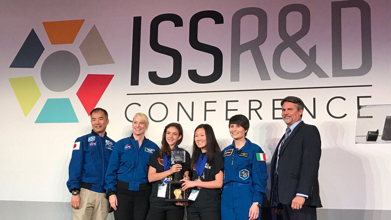 Genes in Space winners Elizabeth Reizis and Sophia Chen pose with astronauts Soichi Noguchi, Kate Rubins, and Samantha Cristoforetti, as well as Mark Mulqueen, ISS Program Manager for Boeing.