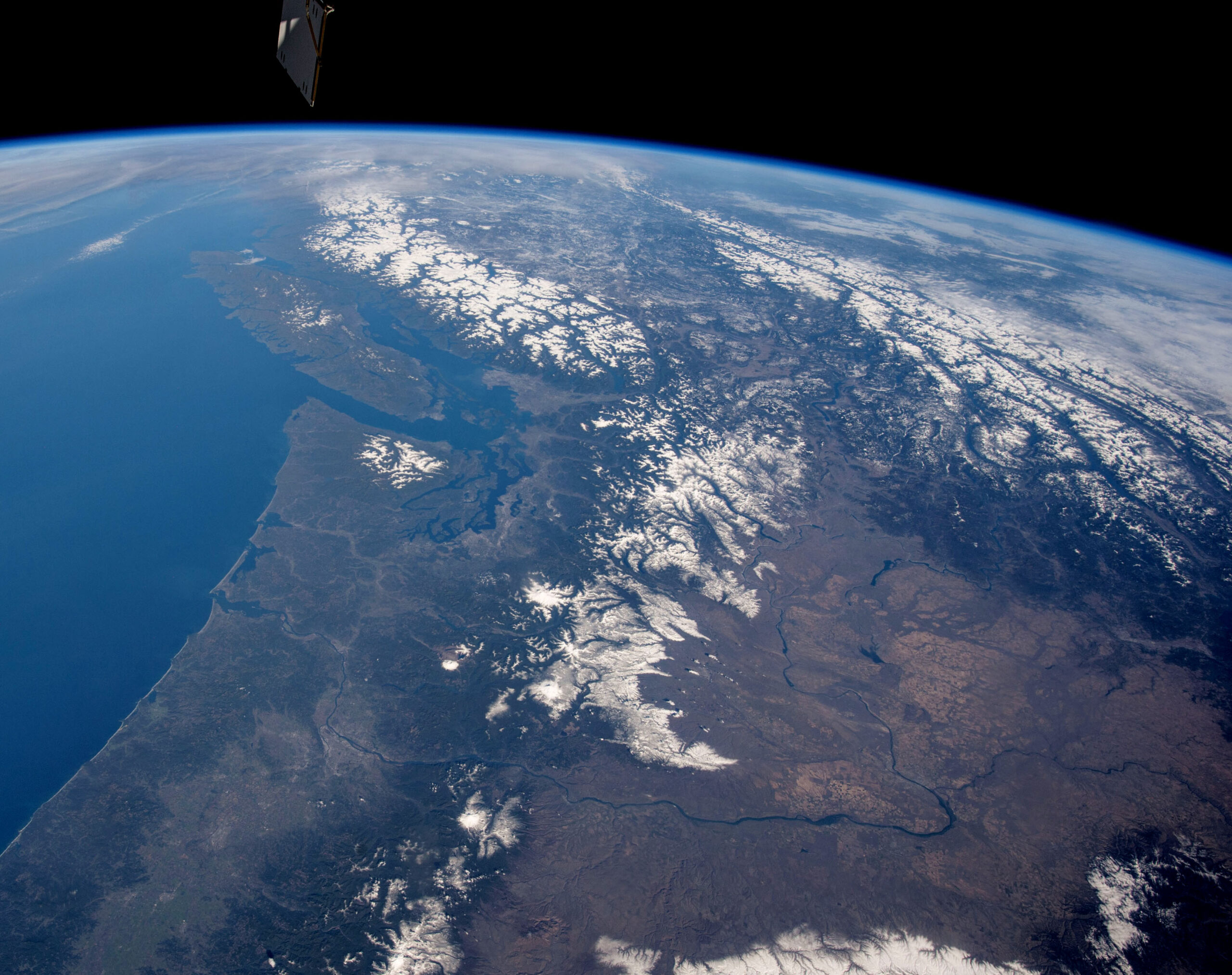 This panoramic photograph was taken by an astronaut looking north from the International Space Station. The snow covered Cascade Range of the U.S. northwest in the foreground gives way to the Rocky Mountains and Coast Mountains in Canada, with Vancouver Island just offshore. Several active volcanoes Mount St. Helens, Mount Rainier and Mount Hood dot the Cascades.