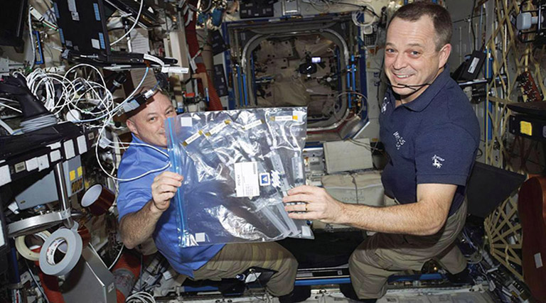 Onboard the ISS, NASA astronauts Scott Tingle and Ricky Arnold hold the KDP experiment developed by Kaitlyn and her team.