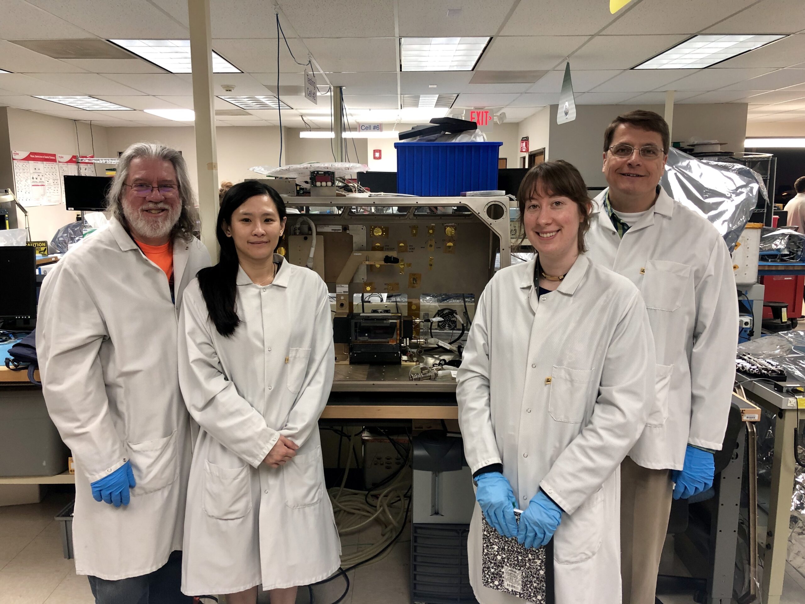 Team members of the Confined Combustion Experiment are shown around the Microgravity Science Glovebox which contains the Confined Combustion hardware.