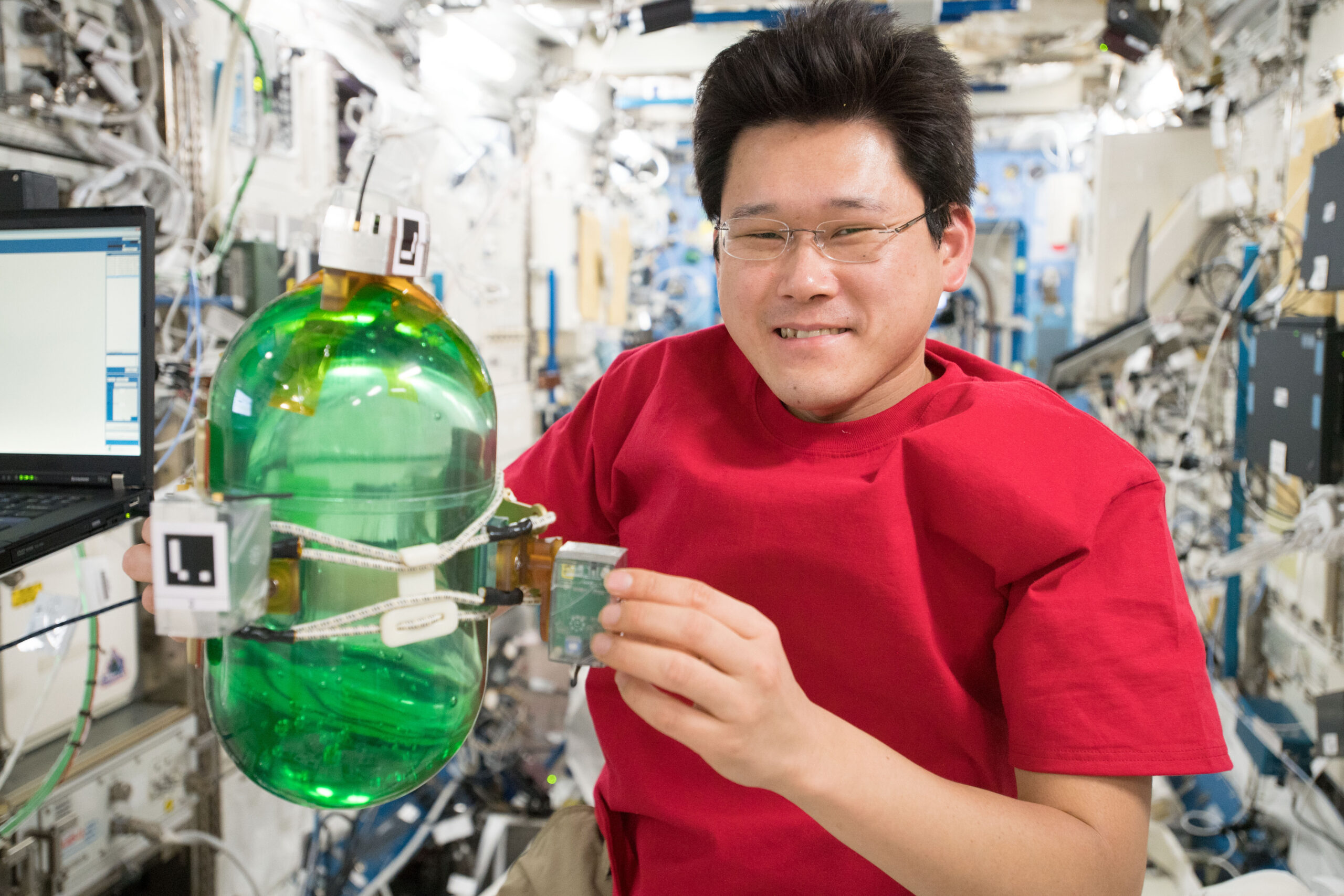Japan Aerospace Exploration Agency (JAXA) astronaut Norishige Kanai works on the Synchronized Position Hold, Engage, Reorient, Experimental Satellites (SPHERES) Tether Slosh experiment, that uses two SPHERES robots tethered to a fluid filled container covered in sensors to test strategies for safely steering spacecraft such as dead satellites that might still have fuel in the tank.