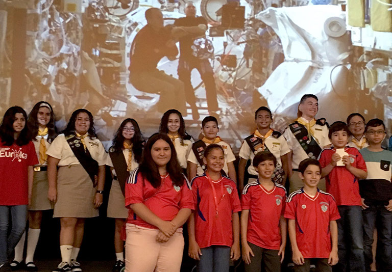 The middle school teams from Puerto Rico pose in front of a screen showing the live webcast from the ISS.