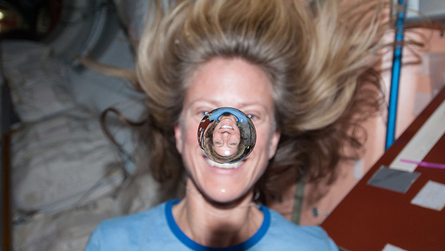 NASA astronaut Karen Nyberg watches a water bubble float freely between her and the camera, showing her image refracted in the droplet.