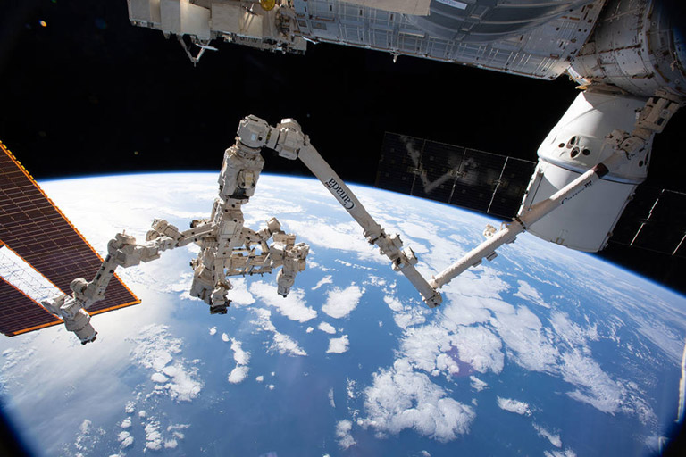 iss059e061425 (May 13, 2019) The Canadarm2 robotic arm with its robotic hand, also known as Dextre, attached for fine tuned robotics work extends across the frame as the International Space Station orbited 256 miles above the Atlantic Ocean. The SpaceX Dragon resupply ship is pictured at right berthed to the Harmony module.