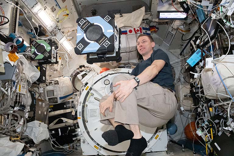 NASA astronaut Eoody Hoburg poses with two of the Astrobees on station.