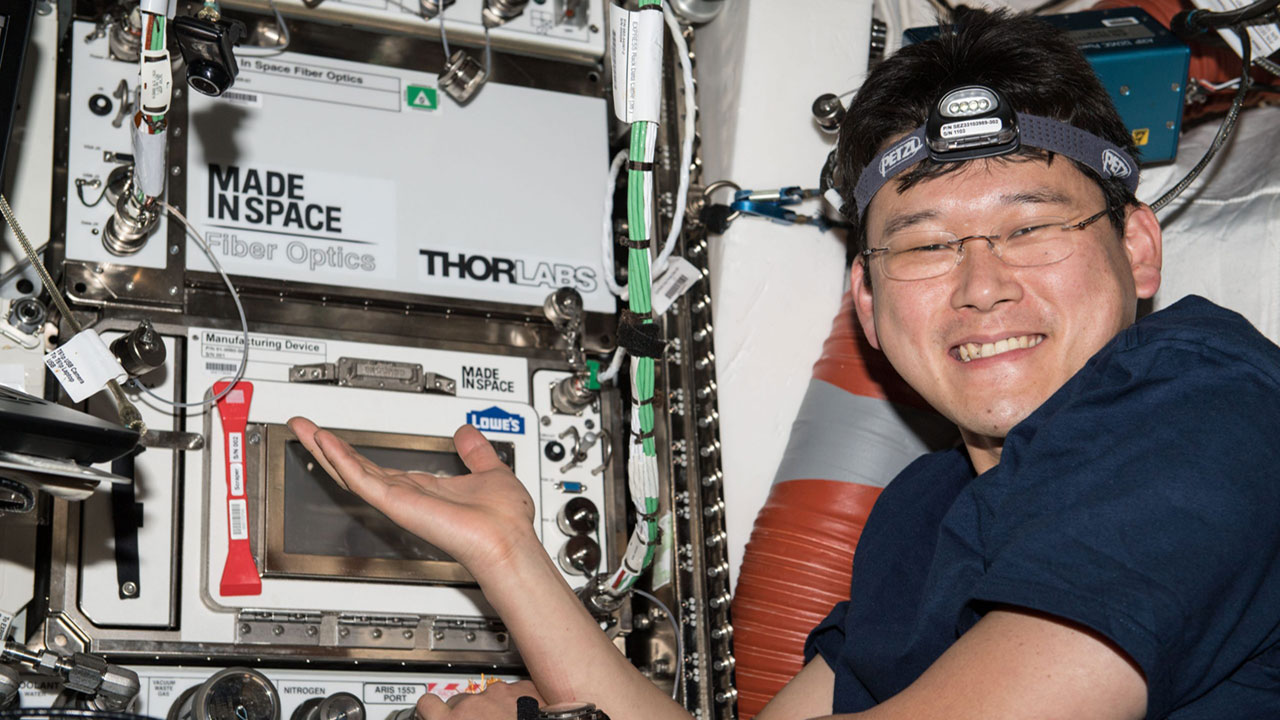 Japan Aerospace Exploration Agency (JAXA) astronaut Norishige Kanai poses for a photo with the installed Made In Space Fiber Optics Locker and the re installed Additive Manufacturing Facility (AMF) Manufacturing Device (ManD). Made In Spaces Optical Fiber Production in Microgravity investigation demonstrates the merits of manufacturing fiber optic filaments in microgravity.