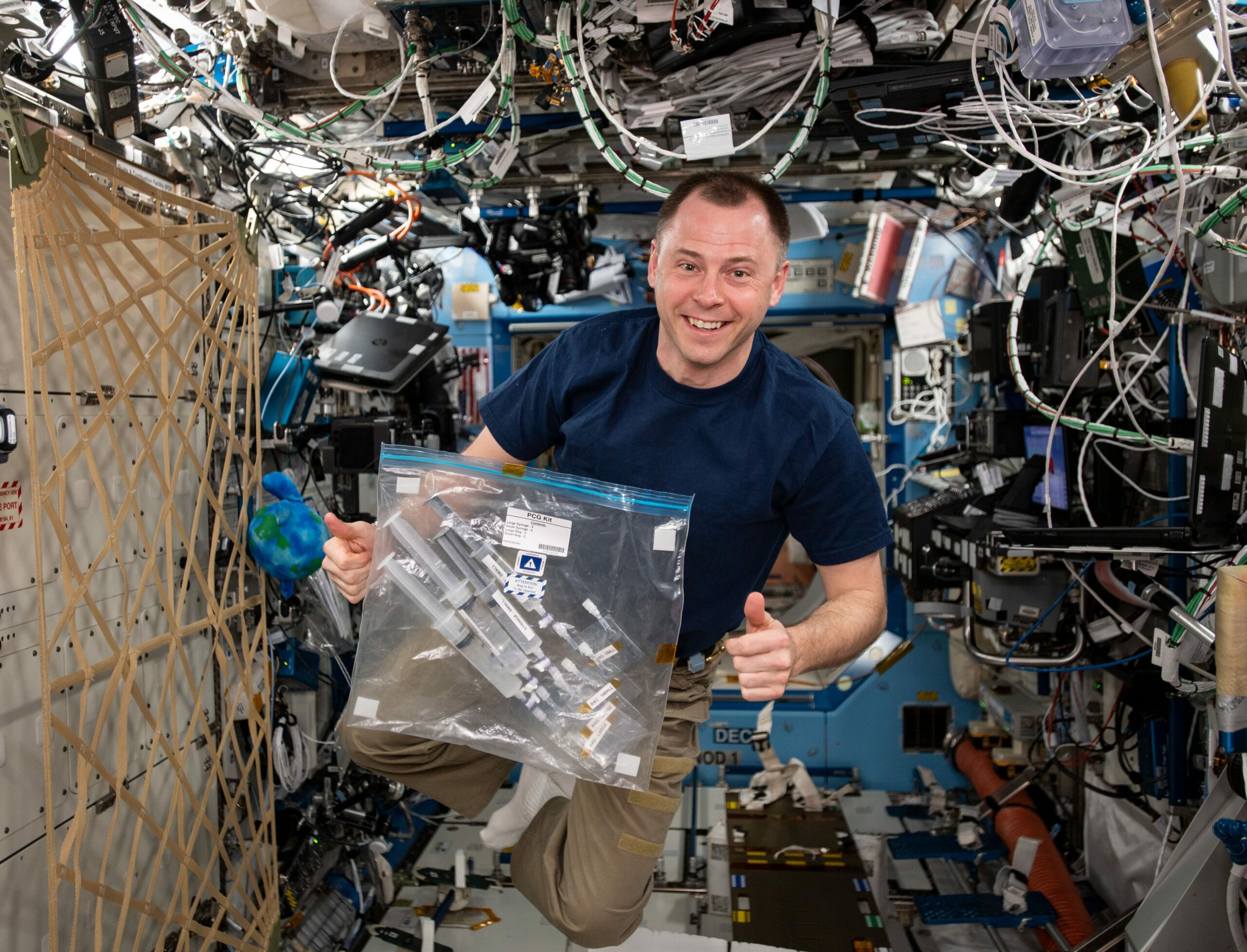 NASA astronaut Nick Hague onboard the ISS holding the PCG Kit bag containing the Wisconsin Space Crystals experiment.