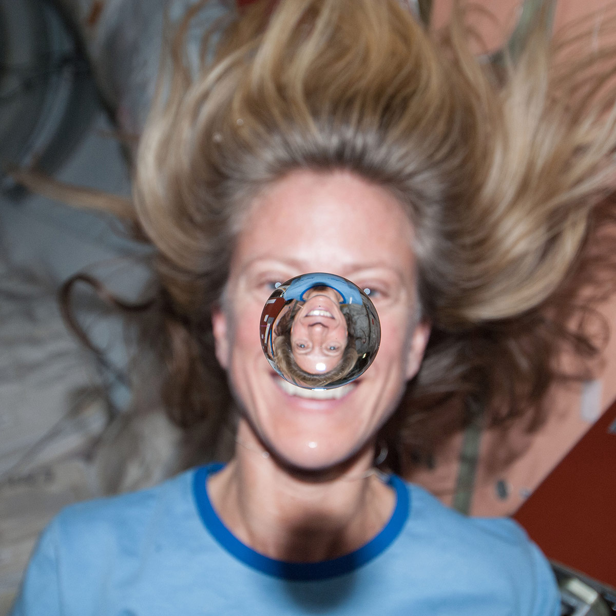 NASA astronaut Karen Nyberg watches a water bubble float freely between her and the camera, showing her image refracted in the droplet.