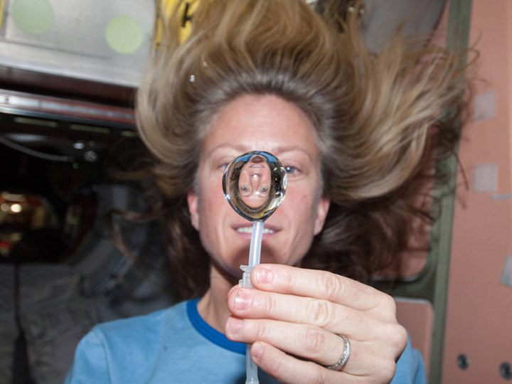 NASA astronaut Karen Nyberg, Expedition 36 flight engineer, squeezes a water bubble out of her beverage container, showing her image refracted, in the Unity node of the International Space Station.