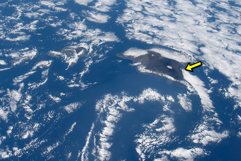 An astronauts photo of Hawaii and the Pacific on June 6, 2018. The arrow points to Kilauea Volcano, where volcanic gases and smoke from forest fires are helping produce dense clouds that drift southward.