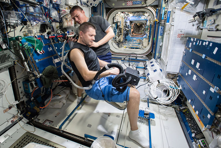 In this 2015 photo, Oleg Kononenko (foreground) and Kjell Lindgren hook their feet under blue handrails to stay put otherwise this haircut might turn out funky. An older type of foot restraint is attached to the handrail on the right.