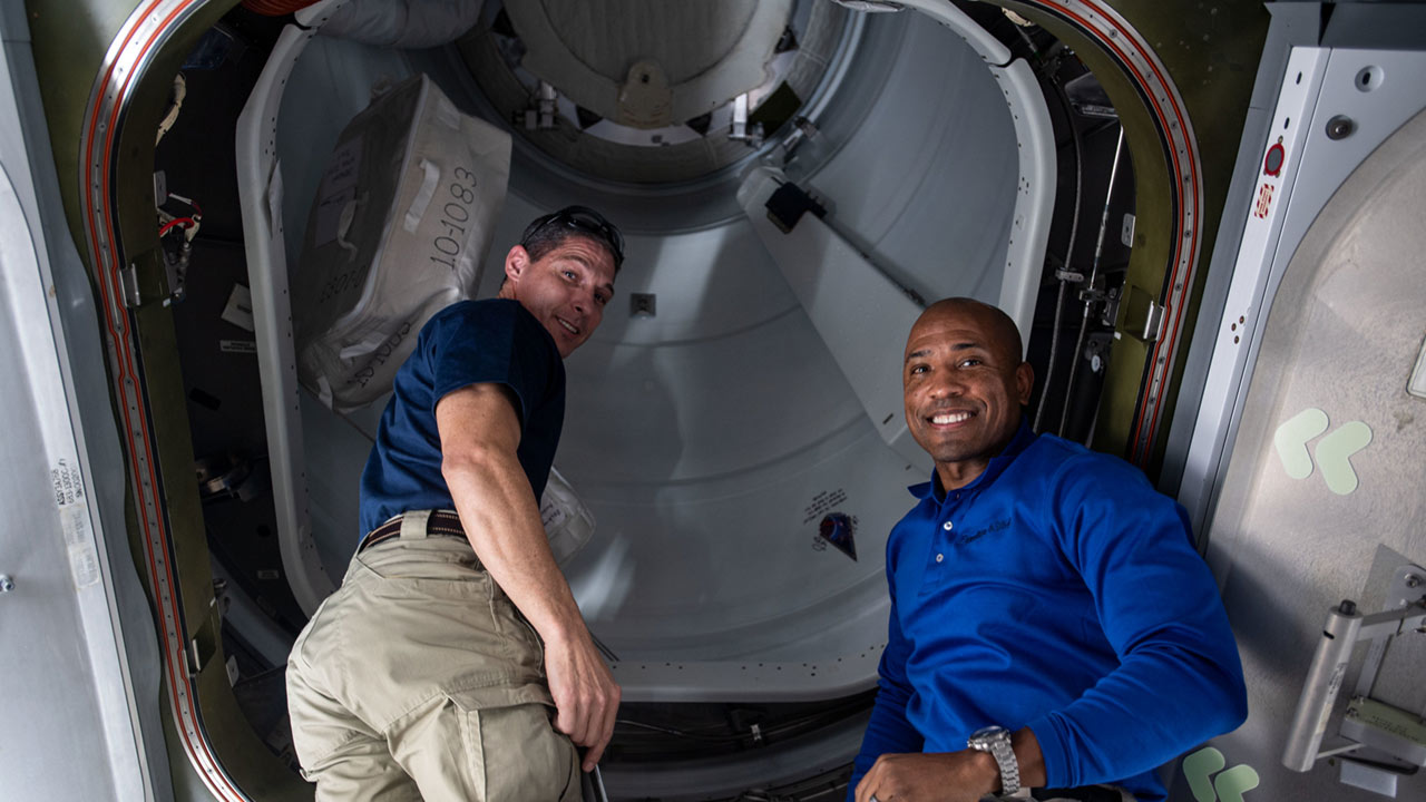 iss064e011087 (Dec. 7, 2020) NASA astronauts (from left) Michael Hopkins and Victor Glover are pictured in the vestibule between the Harmony module and the International Docking Adapter 3 before opening the hatch to the newly docked SpaceX Cargo Dragon vehicle.