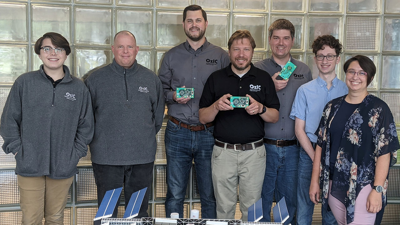 The seven member team that developed the UV XNode holding the UV detector and a model of the ISS in front of them.