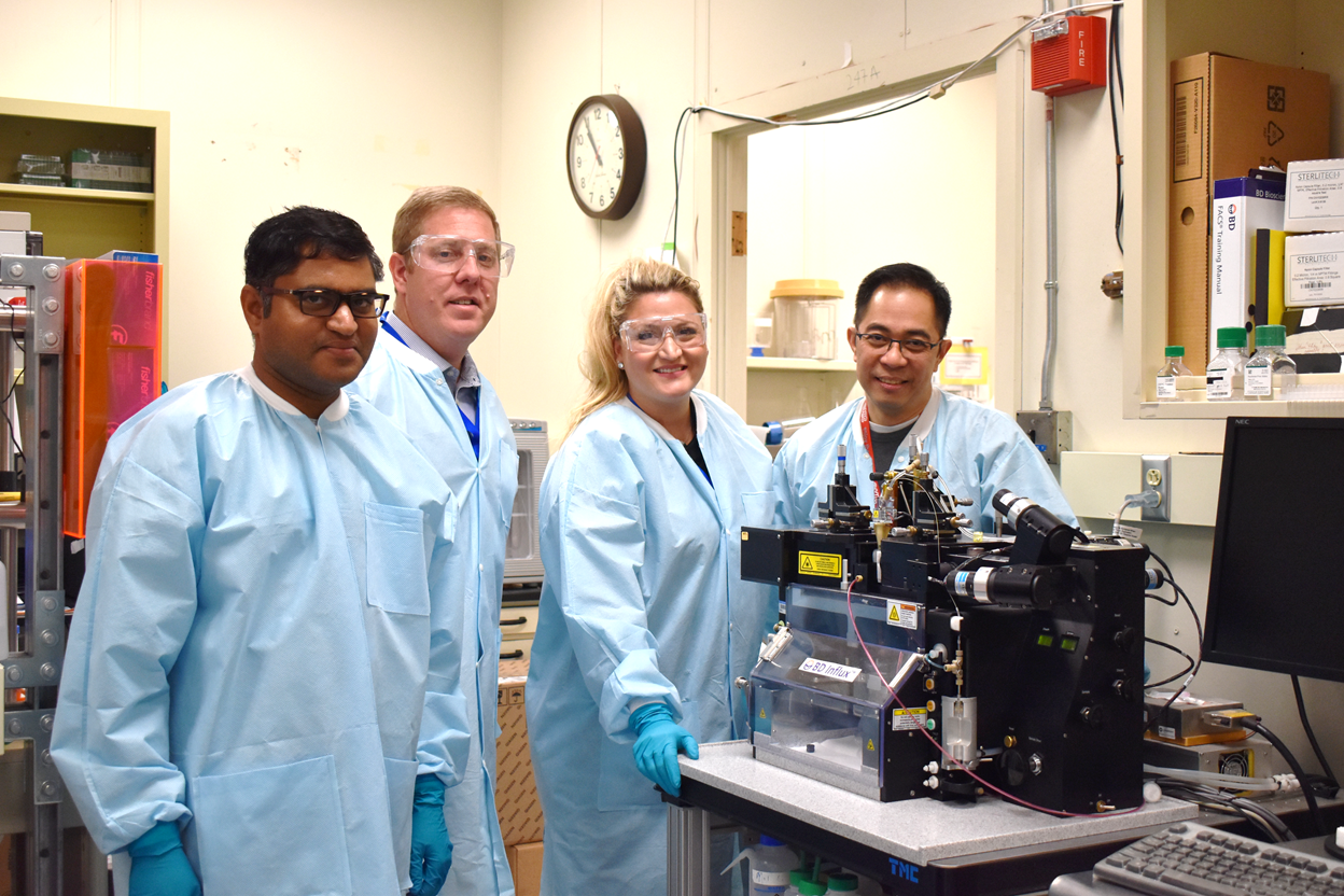 The Space Microbiome team pictured with the flow cytometer at Los Alamos National Lab that will analyze the space samples upon return (left to right: Anand Kumar, Heath J. Mills, Olivia G. Holzhaus, Armand Dichosa)