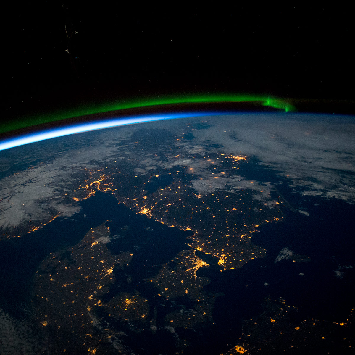 Astronauts aboard the International Space Station took this photograph of southern Scandinavia just before midnight on April 3, 2015. Prominent features include a green aurora to the north, the blackness of the Baltic Sea (lower right), and clouds (top right) and snow (in Norway) illuminated by the full Moon. City lights clearly show the coastline of the Skagerrak and Kattegat seaway that separates Denmark from its neighbors to the north and leads into the Baltic Sea. The largest light clusters on the seaway are the capital cities of Oslo and Copenhagen. Cities facing the Baltic are the Polish port of Gdansk and the Swedish capital, Stockholm. Smaller cities in northern Germany also trace the Baltic coastline (lower right).