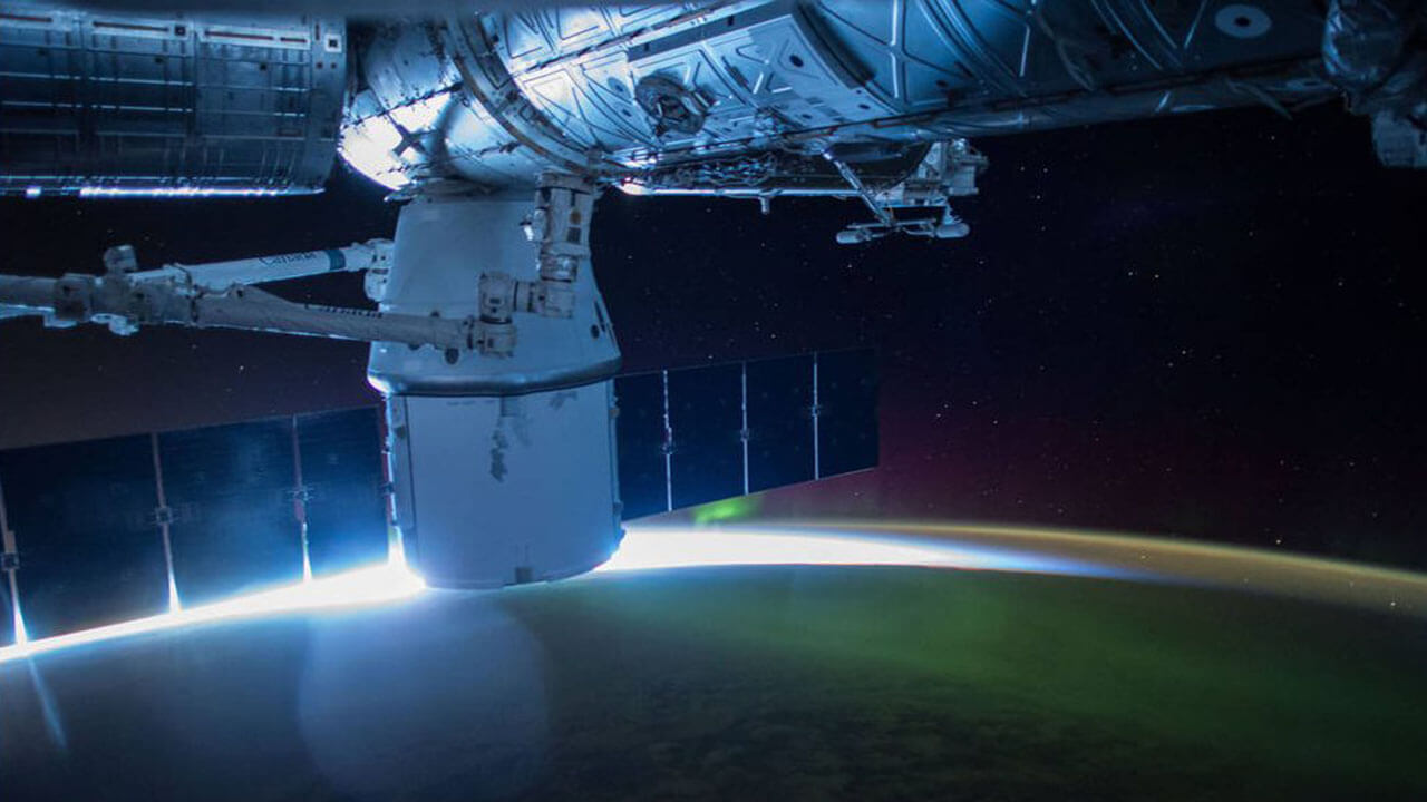 This night image from the International Space Station shows the sun beginning to peak above the horizon sparkling through a green Aurora and reflecting a blue reflection off the station on Apr. 18, 2015 during Expedition 43.