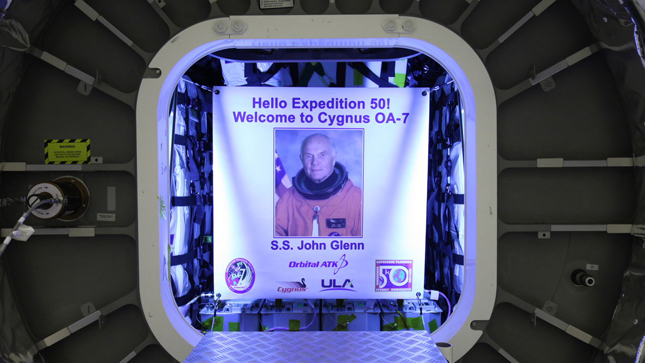 Inside the Payload Hazardous Servicing Facility at NASAs Kennedy Space Center in Florida, the John Glenn banner is attached inside the Orbital ATK Cygnus pressurized cargo module. The Cygnus cargo module has been renamed the S.S. John Glenn to honor the late former Project Mercury and space shuttle astronaut.