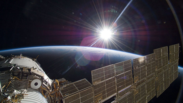 The bright sun greets the International Space Station and the Earth below.