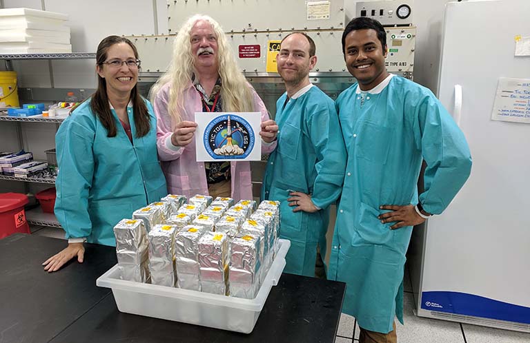 The Gilroy Lab research team at the Kennedy Space Center as they hand over the TIC TOC experiment for launch: (right to left) Sarah Swanson, Simon Gilroy, Richard Barker, and Arkadipta Bakshi.