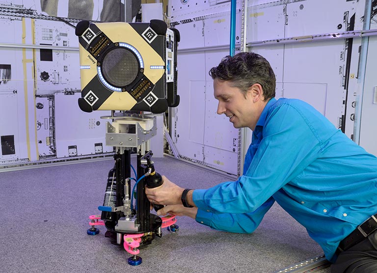 Jonathan Barlow working with an Astrobee flight unit, Honey, on the granite table lab at the Automated Science Research Facility at NASA Ames Research Center.