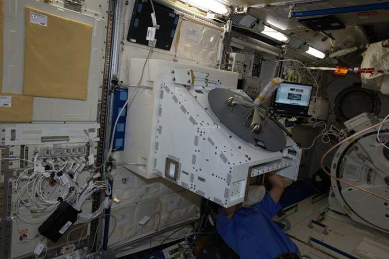 Astronaut installing a payload on the NREP inside the ISS. The NREP hosts payloads and has mechanical, electrical, and data interfaces.