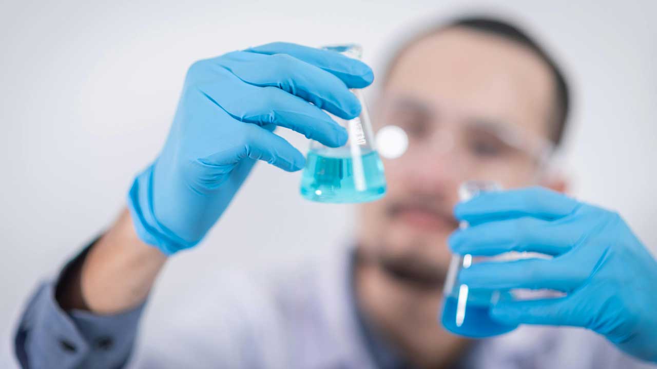 returning-investigator-blue Male scientist mixing liquid in beakers