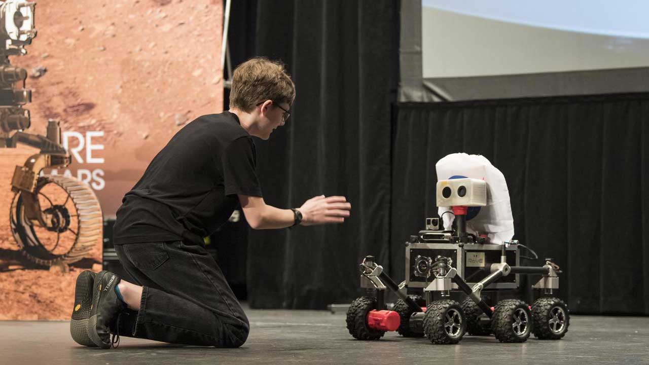 rov-e-mars-rover ROV-E, a new Mars outreach rover, rolls toward Alex Mather, the student whose submission, Perseverance, was chosen as the official name of the Mars 2020 rover, with NASA handouts at an event to announce the official name of the rover, Thursday, March 5, 2020
